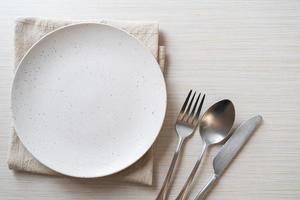 Empty plate or dish with knife, fork, and spoon on wood tile background photo