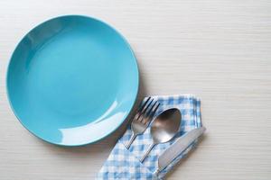 Empty plate or dish with knife, fork, and spoon on wood tile background