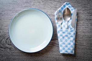 Empty plate or dish with knife, fork, and spoon on wood tile background photo