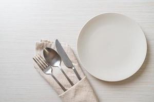 Empty plate or dish with knife, fork, and spoon on wood tile background photo