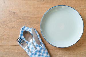 Empty plate or dish with knife, fork, and spoon on wood tile background photo