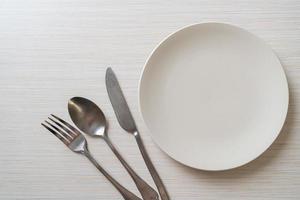 Empty plate or dish with knife, fork, and spoon on wood tile background photo