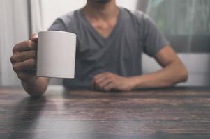 Hombre sosteniendo un vaso de agua, una taza de café, sobre un escritorio, en su oficina. foto