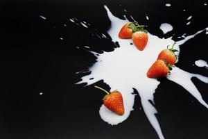 A group of strawberries with splash milk on the balck background photo