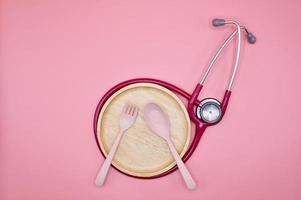 A pink stethoscope with wooden dish, spoon and fork on the pink background photo