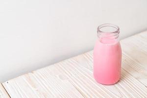 Pink milk or strawberry milk in bottle on wood background photo