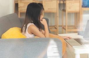 A young asian girl  using computer to leran at home as social distancing protocol during covid-19 or coronavirus pandemic. home schooling concept photo