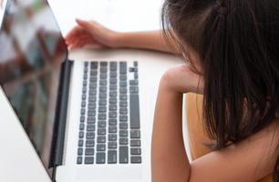 A young asian girl  using computer to leran at home as social distancing protocol during covid-19 or coronavirus pandemic. home schooling concept photo