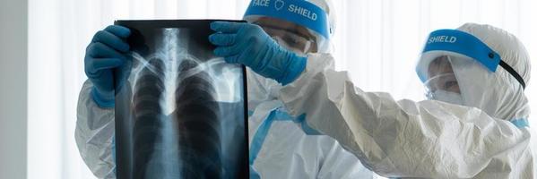 Doctor and nurse in personal protective equipment or ppe looking at chest x-ray of the asian woman patient with covid-19 or coronavirus infection in the isolation unit in the hospital. medical concept photo