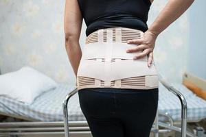 Asian lady patient wearing back pain support belt for orthopedic lumbar with walker. photo