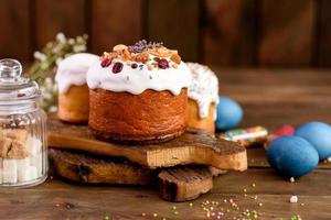 Festive cakes with white glaze, nuts and raisins with Easter eggs on the festive table photo