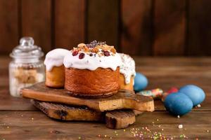 Festive cakes with white glaze, nuts and raisins with Easter eggs on the festive table photo