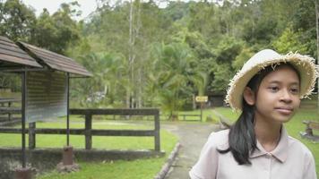 Linda jovencita con sombrero de paja caminando tranquilamente y disfrutando de ver el hermoso paisaje en el parque forestal durante el verano. tailandia video