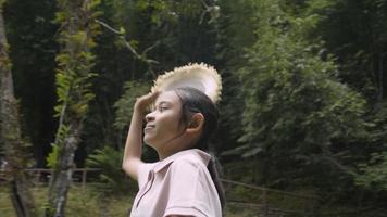 tournant autour d'une joyeuse fille asiatique portant un chapeau de paille regardant autour d'un parc forestier à feuillage luxuriant. vacances d'été. voyage d'excursion. Thaïlande. video