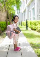 Niña con libro y mochila caminando en el parque listo para volver a la escuela foto