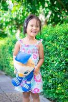 Retrato de feliz niña asiática con muñeca de pie en la acera en el parque foto