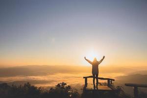 El hombre levanta la mano en la cima de la montaña y la puesta del sol, la libertad y el concepto de aventura de viaje. creencias religiosas, copie el espacio. foto