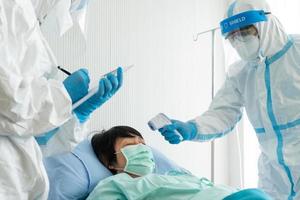 Doctor and nurse in personal protective equipment or ppe treating the asian woman patient with covid-19 or coronavirus infection in the isolation unit in the hospital during pandemic. medical concept photo