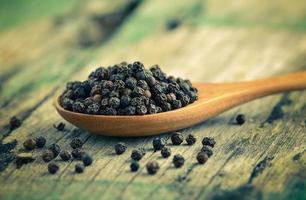 Whole black pepper on wooden spoon photo