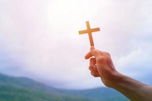 Man praying with cross, while holding a crucifix symbol with bright sunbeam on the sky. photo