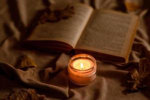 una vela encendida en una mesa de madera frente a un libro a media asta