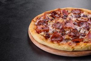 Deliciosa pizza recién horneada con tomates, salami y tocino sobre un fondo de hormigón oscuro foto