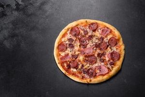 Delicious fresh oven pizza with tomatoes, salami and bacon on a dark concrete background photo