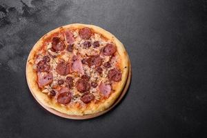 Delicious fresh oven pizza with tomatoes, salami and bacon on a dark concrete background photo