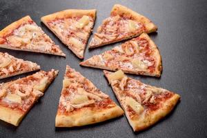 Sabrosa pizza recién horneada con tomate, queso y piña sobre un fondo de hormigón oscuro foto