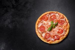 Tasty fresh oven pizza with tomatoes, cheese and basil on a concrete background photo