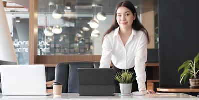 Confianza empresaria de pie en su escritorio de oficina y sonriendo a la cámara. foto