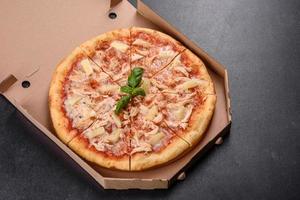 Sabrosa pizza recién horneada con tomate, queso y piña sobre un fondo de hormigón oscuro foto