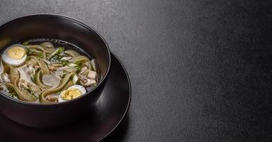 Deliciosa sopa caliente fresca con fideos y huevo de codorniz en una placa negra foto