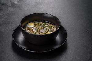 Fresh delicious hot soup with noodles and quail egg in a black plate photo