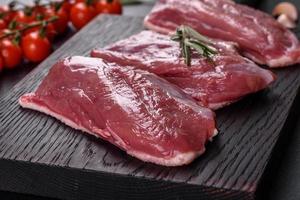 Raw duck breast with herbs and spices on a dark concrete background photo