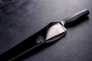 Un gran cuchillo de caza artesanal acostado sobre un fondo oscuro foto