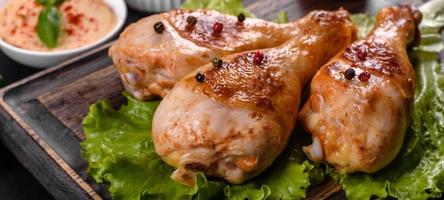 Tasty grilled chicken legs with spices and herbs on a wooden board on a dark concrete background photo