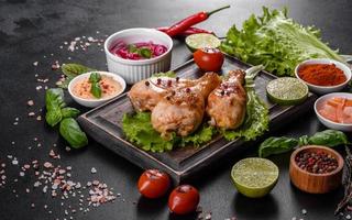 Tasty grilled chicken legs with spices and herbs on a wooden board on a dark concrete background photo