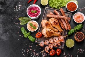 Composition of sausages, chicken, pork and shrimp prepared on grill, as well as vegetables prepared on grill with spices and herbs photo