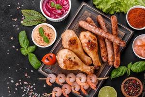 Composition of sausages, chicken, pork and shrimp prepared on grill, as well as vegetables prepared on grill with spices and herbs photo