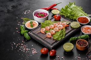 Tasty freshly prepared shrimp with spices and herbs on a wooden board on a dark concrete background photo