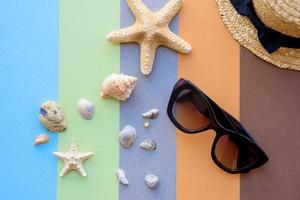 Glasses and hat with shells and sea stars on a colored background photo