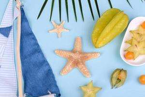 Fruit carambol, beach accessories and foliage of a tropical plant on colored paper photo