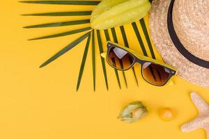 Fruit carambol, beach accessories and foliage of a tropical plant on colored paper photo