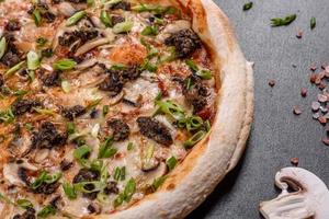 Fresh delicious Italian pizza with meat, mushrooms and tomatoes on a dark concrete background photo