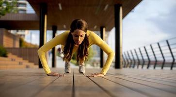 Young woman performing pushups at wooden walkway by the river photo