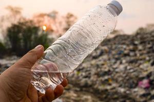 Plastic bottle in man hand on large garbage pile and pollution background photo