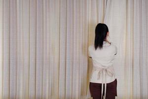 Housemaid closing the curtains on window In hotel room photo