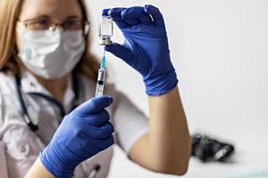 A female doctor wearing a medical mask draws the coronavirus vaccine into a syringe at the clinic.The concept of vaccination, immunization, prevention against Covid-19. photo