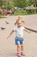 Little girl toddler runs after pigeons. Summertime photo